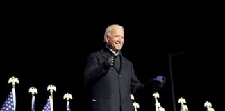 Joe Biden in front of American flags, black background | Licas News
